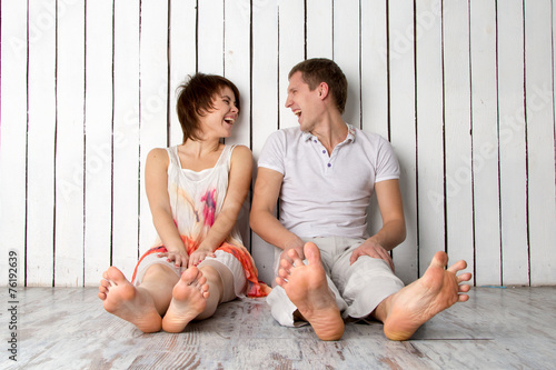 Young couple is laughing near the white wooden wall