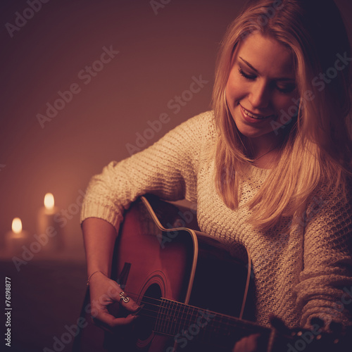 Young blonde woman playing guitar in candle light photo