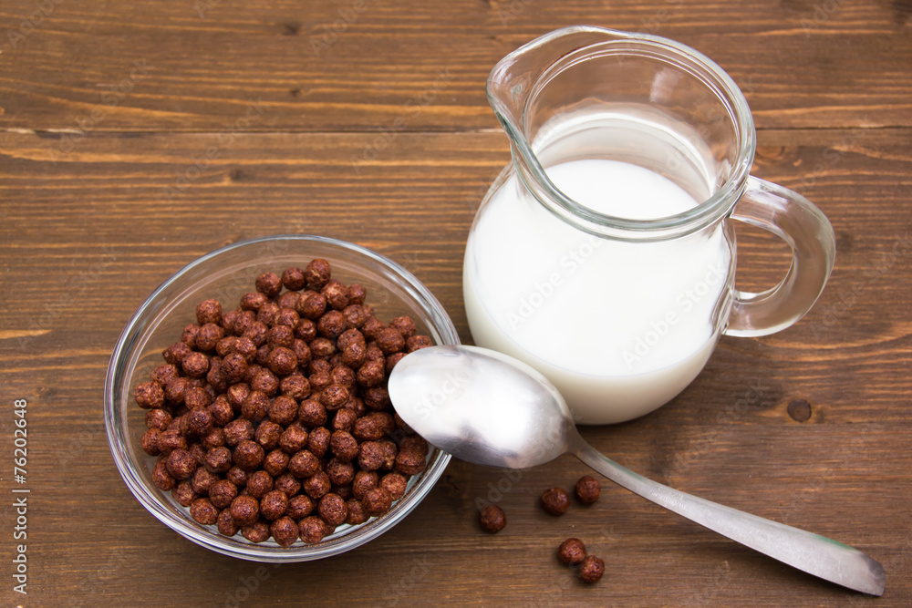 Bowl with chocolate cereals and milk jug on wood from above Bowl with chocolate cereals and milk jug on wood from above
