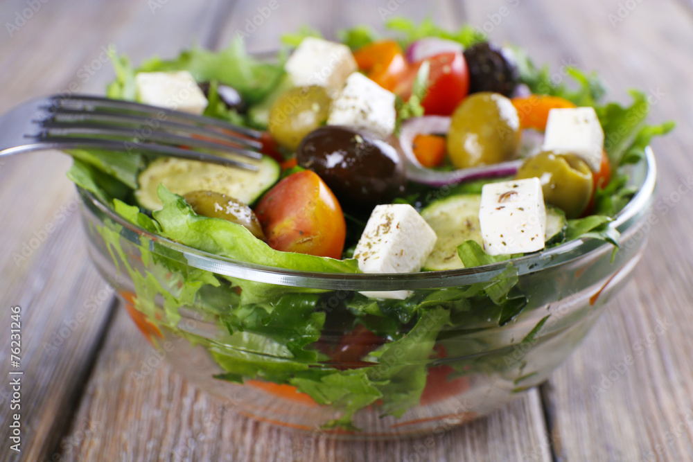 Greek salad in glass dish with fork on wooden background Greek salad in glass dish with fork on wooden background