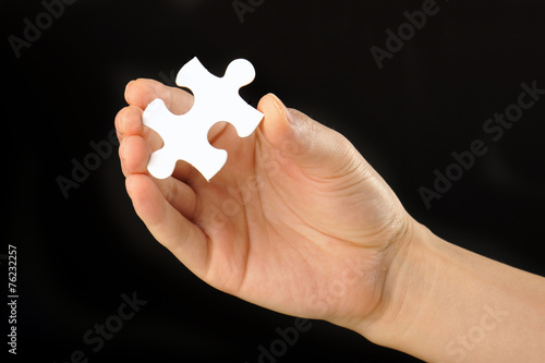 黒い背景で白いパズルのピースを持っている人間の手