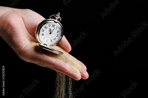 Silver pocket clock in hands and sand flowing away