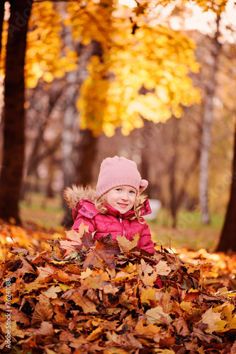 adorable smiling child girl sitting in leaves in autumn park