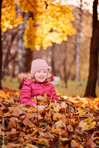 adorable child girl sitting in leaves in autumn park