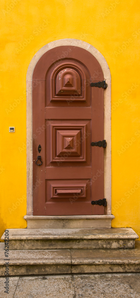 Old wooden door with metal hinges and lock on the yellow wall