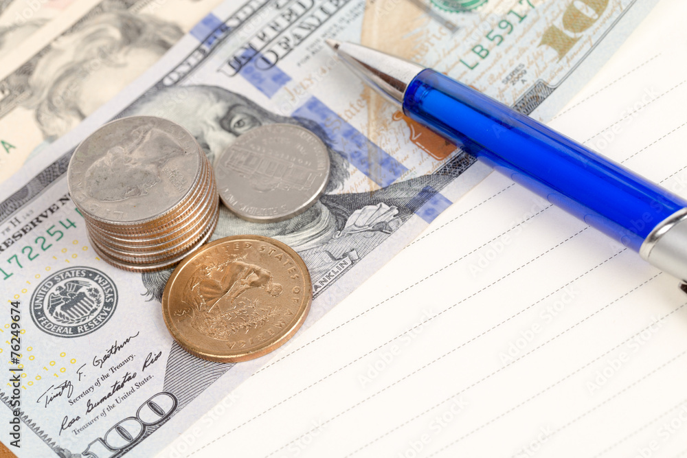 US coins and banknotes with pen on a notebook US coins and banknotes with pen on a notebook