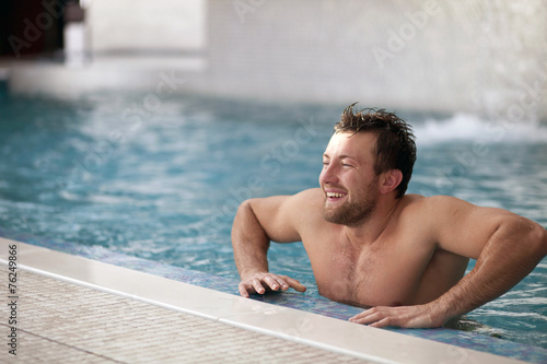 Young man leaning at edge of swimming pool 