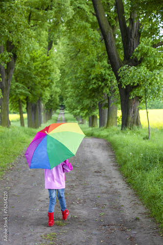 little girl wearing rubber boots with umbrella in spring alley