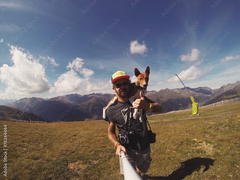 Man hikes in mountains with his dog on his shoulders - obrazy, fototapety, plakaty 