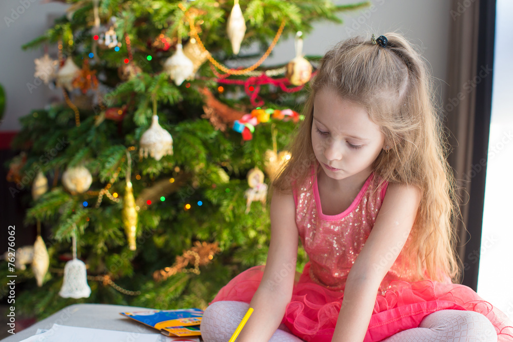 Adorable little girl drawing near Christmas tree