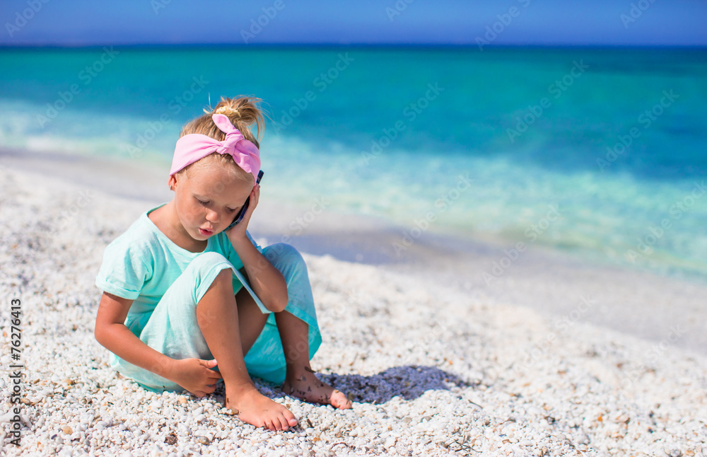 Little adorable girl talking at phone during beach vacation