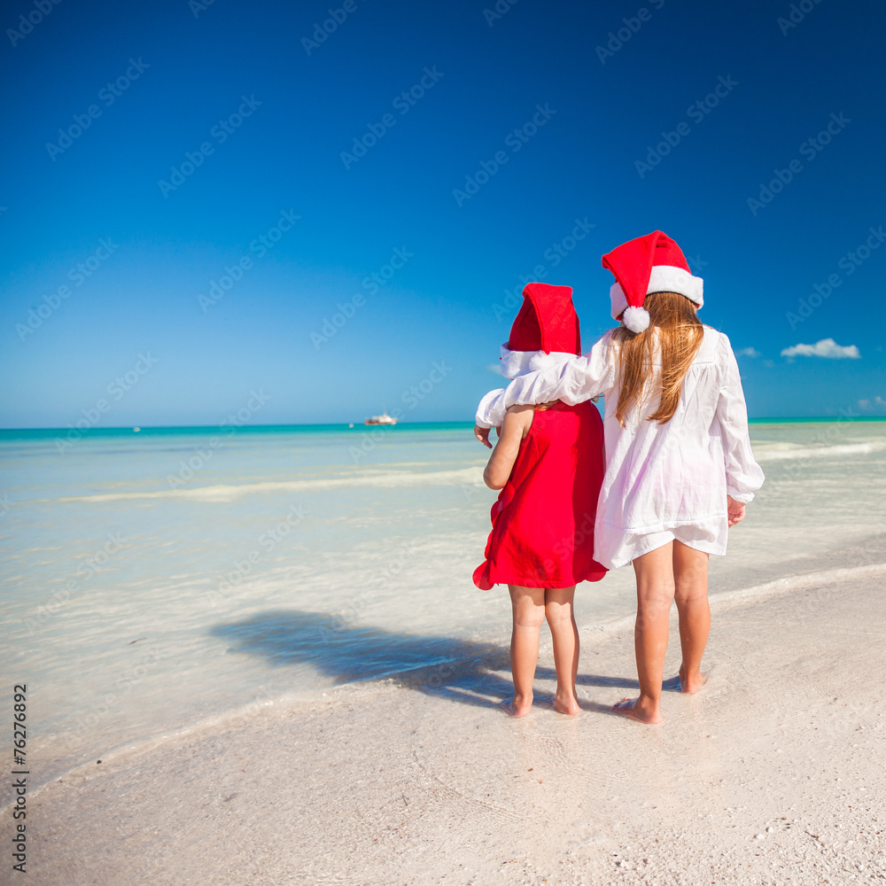 Little adorable girls in Santa hats during beach vacation Little adorable girls in Santa hats during beach vacation