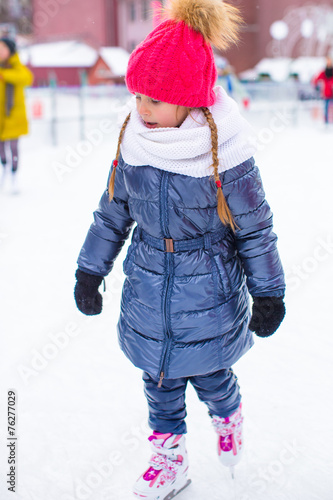 Adorable little girl skating on the ice rink outdoors