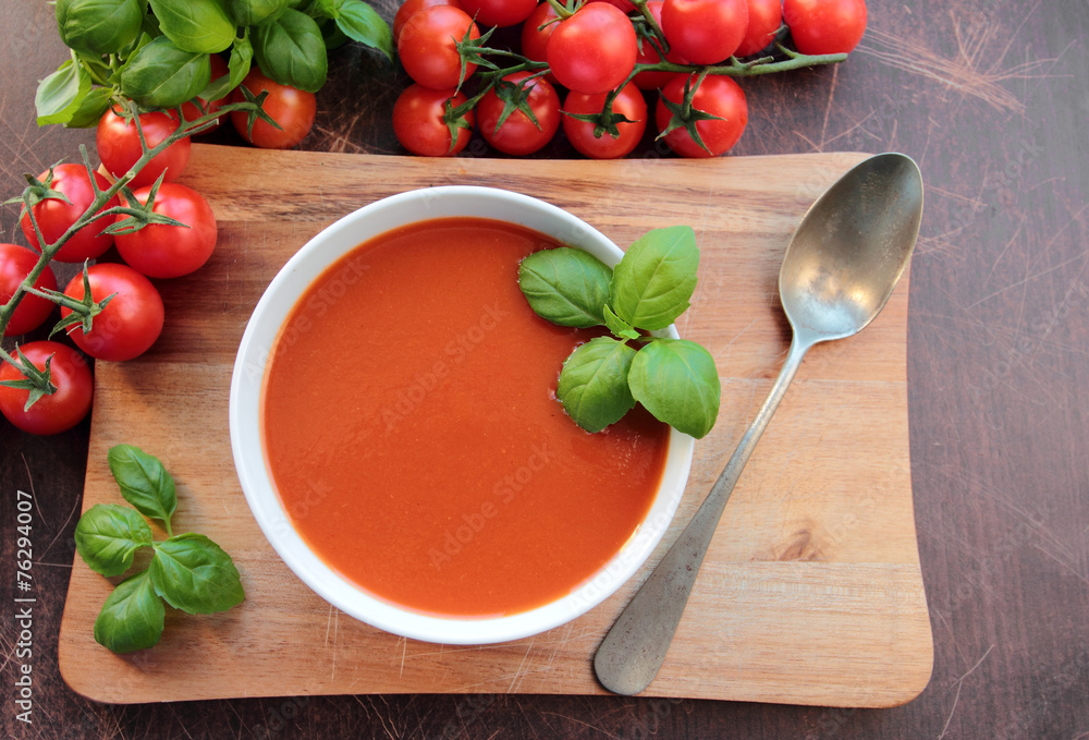 Tomato soup in a bowl on wooden board with spoon Tomato soup in a bowl on wooden board with spoon