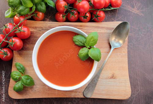 Tomato soup in a bowl on wooden board with spoon