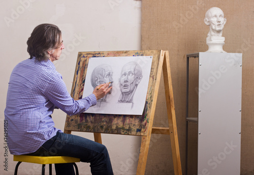 A man draws a pencil sitting at his easel.