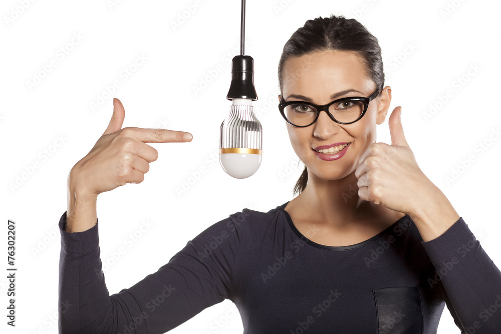young woman pointing on LED bulb and showing thumbs up young woman pointing on LED bulb and showing thumbs up