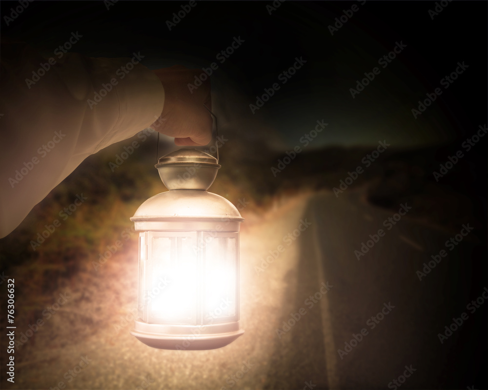 Hand holding light illuminating dark road at night