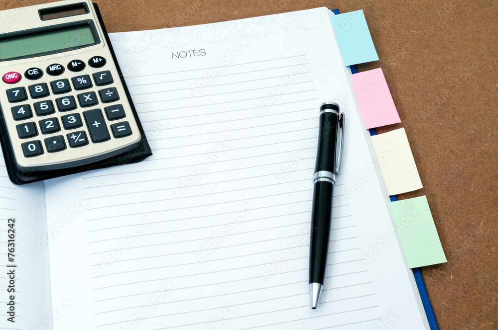 Blank notebook page with black ball pen and calculator on top Blank notebook page with black ball pen and calculator on top