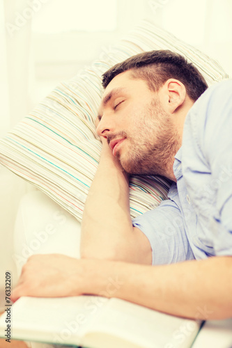 calm young man lying on sofa at home with book