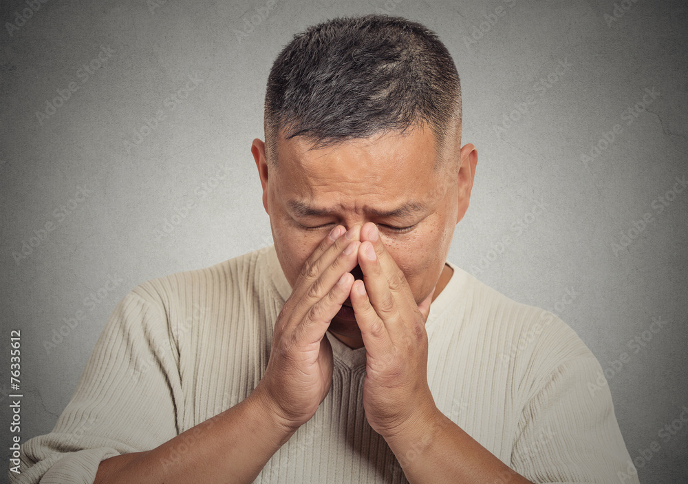 Headshot sad young man looking down grey wall background 
