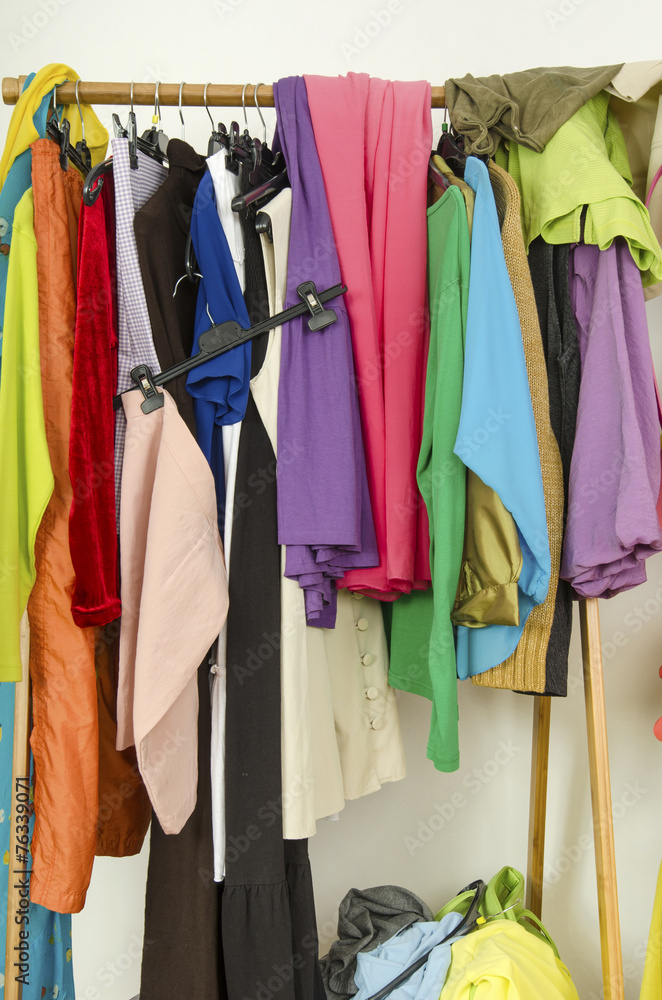 Untidy messy cluttered woman wardrobe with colorful clothes.