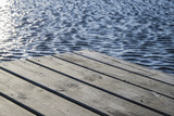 Fragment pomostu nad jeziorem i odbijające się w wodzie słońce