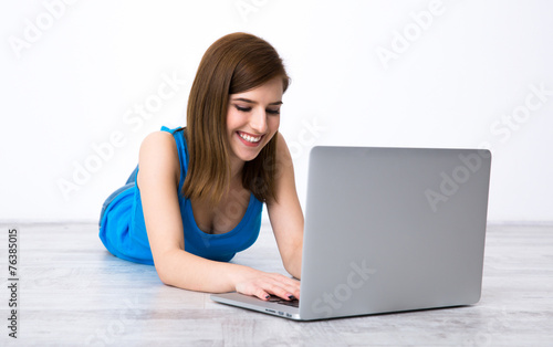 Happy beautiful woman lying on the floor with laptop