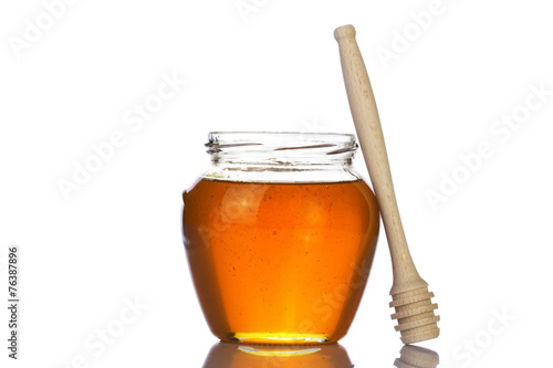 Glass jar of honey with wooden drizzler on a white background.
