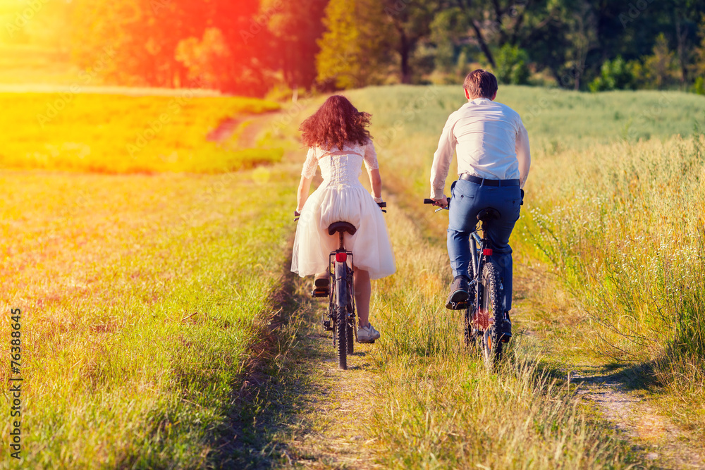 Obraz premium Young happy bride and groom ride bicycles in the meadow