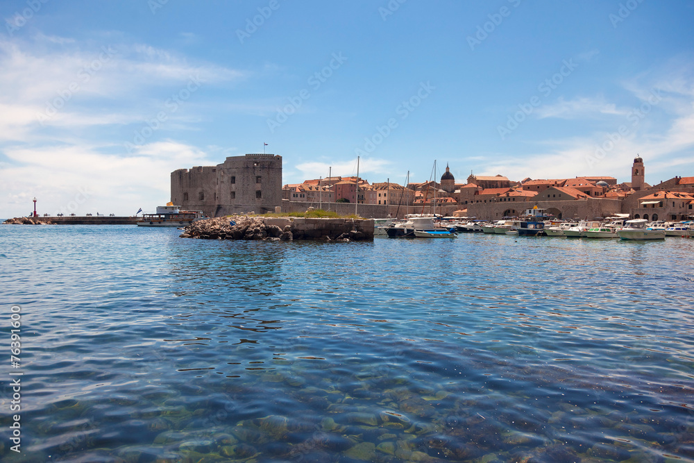 Small boats in city port with St. John fortress in background.