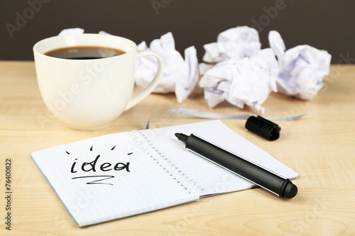Cup of coffee with crumpled paper and note Idea in notebook