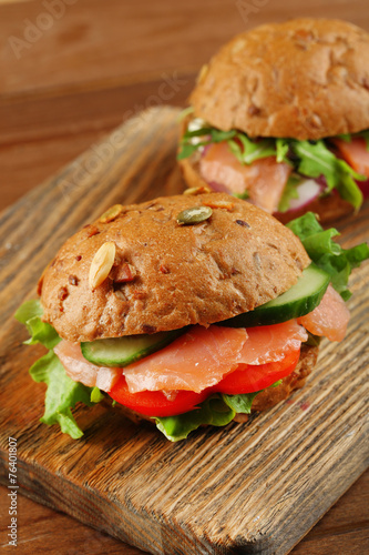 Sandwiches with salmon on cutting board, on wooden background