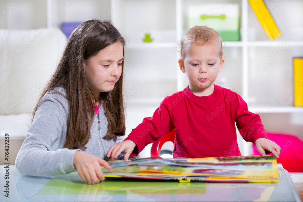 Two smiling children reading the book on the desk Two smiling children reading the book on the desk