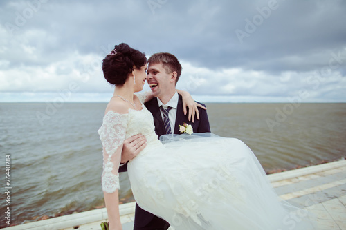 Groom holding bride in his arms by the sea 