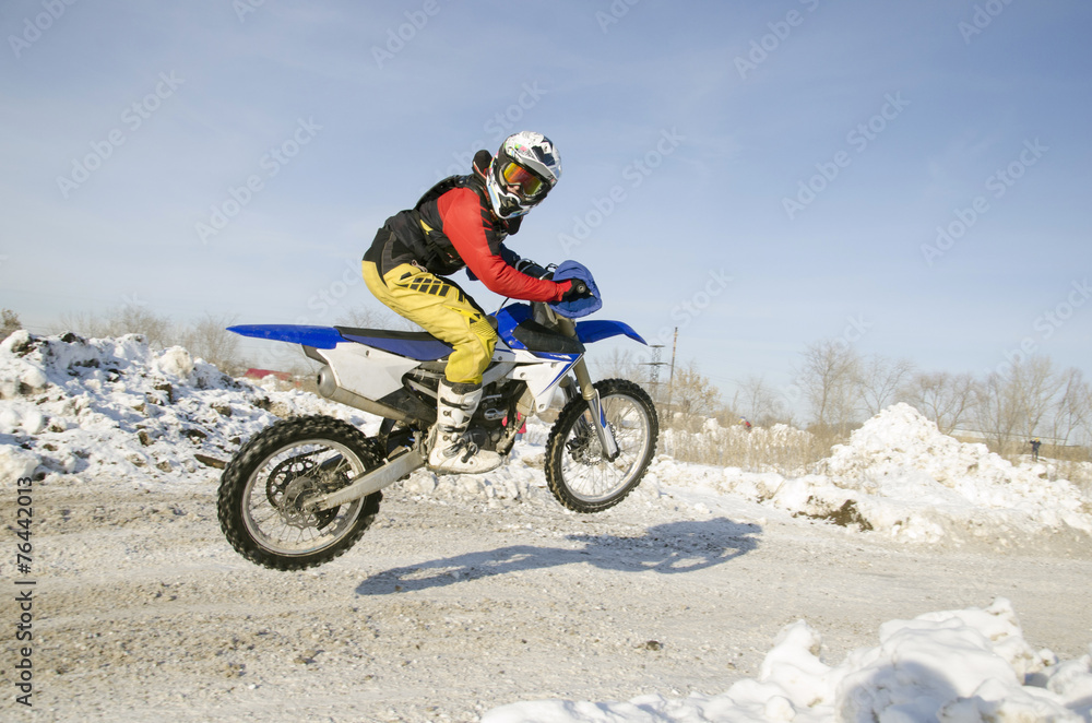 MX winter rider soars from a hill looking back