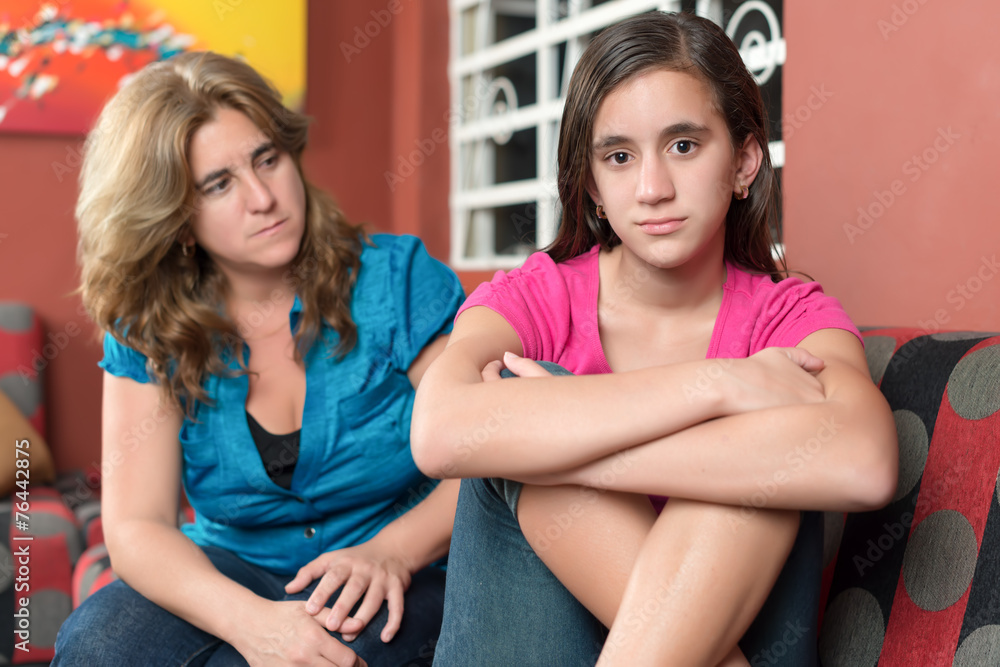 Worried and sad mother looks at her defiant teen daughter