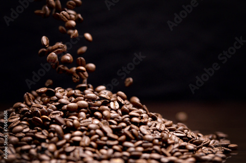 High contrast image of coffee beans being dropped onto pile with
