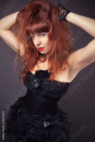 gothic redhead woman in sexy black satin corset against dark gre