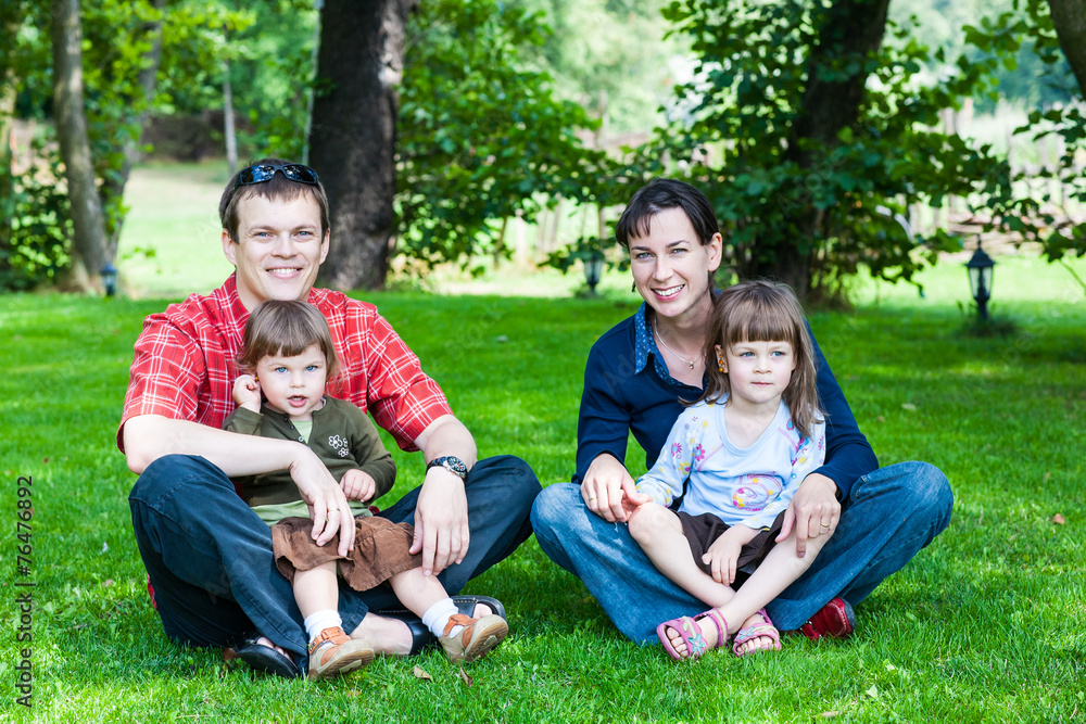Happy family of four sitting on grass