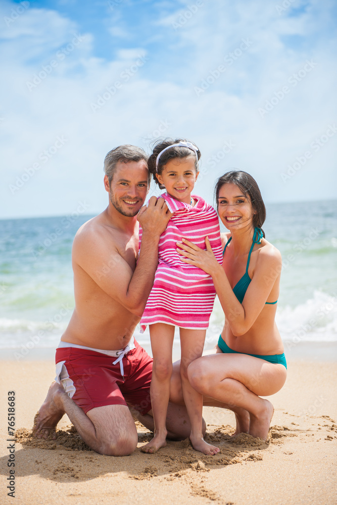A couple at the beach posing in swimsuits with their daughter A couple at the beach posing in swimsuits with their daughter