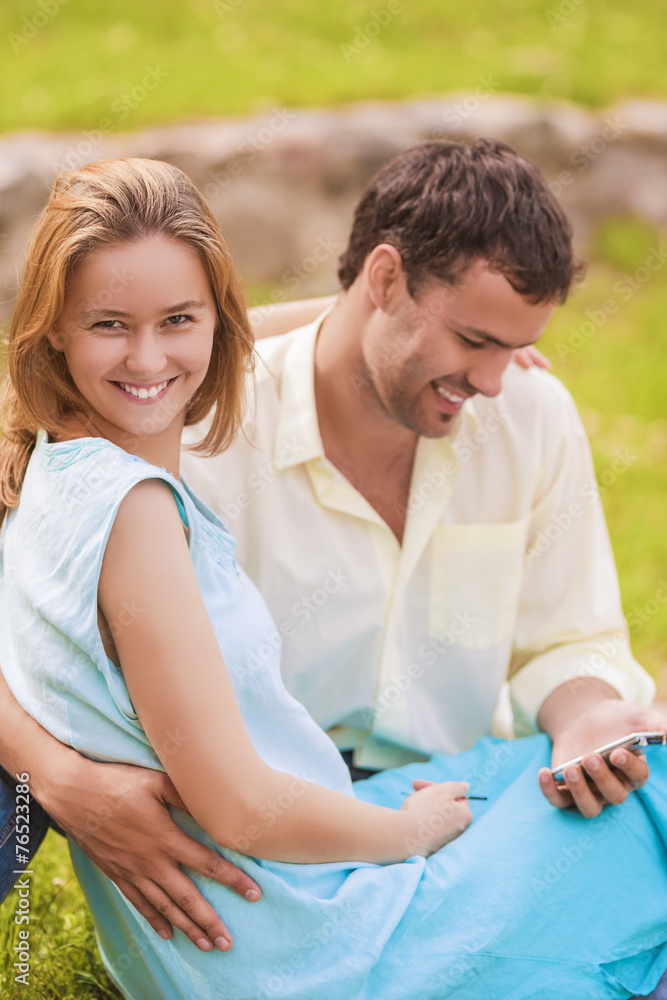 Happy caucasian Couple Sitting Together Outdoors While Using PDA Happy caucasian Couple Sitting Together Outdoors While Using PDA