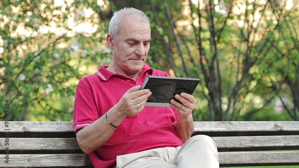 Retired senior man resting and using his tablet at table in park Retired senior man resting and using his tablet at table in park