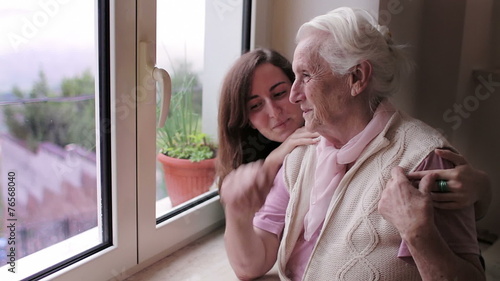 Grandmother And Granddaughter Relaxing near windown at sunset At Home - hug  photo