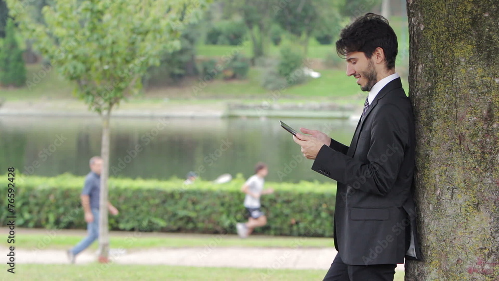 Young businessman at the park beneath the tree using tablet Young businessman at the park beneath the tree using tablet