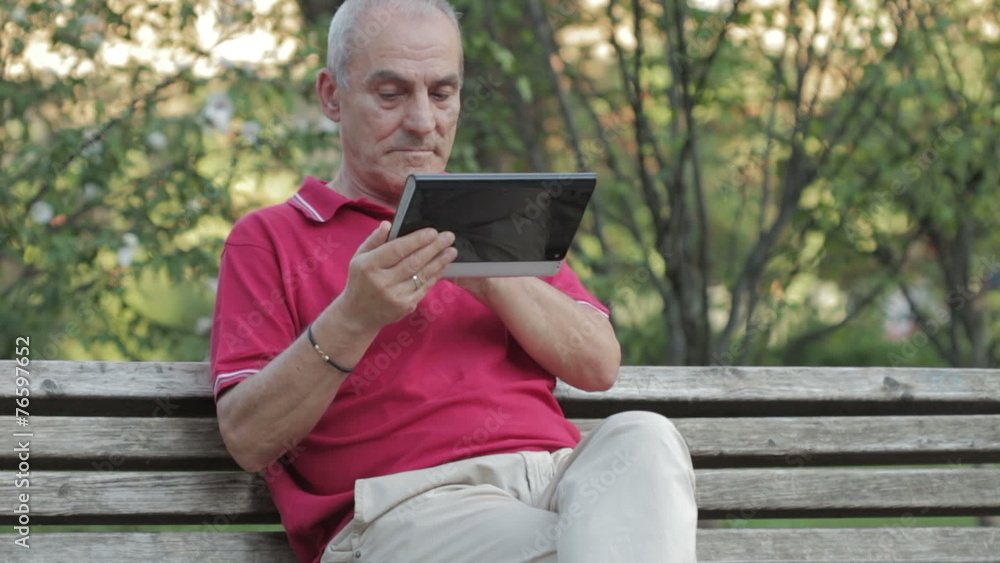Retired senior man resting and using his tablet at table in park Retired senior man resting and using his tablet at table in park