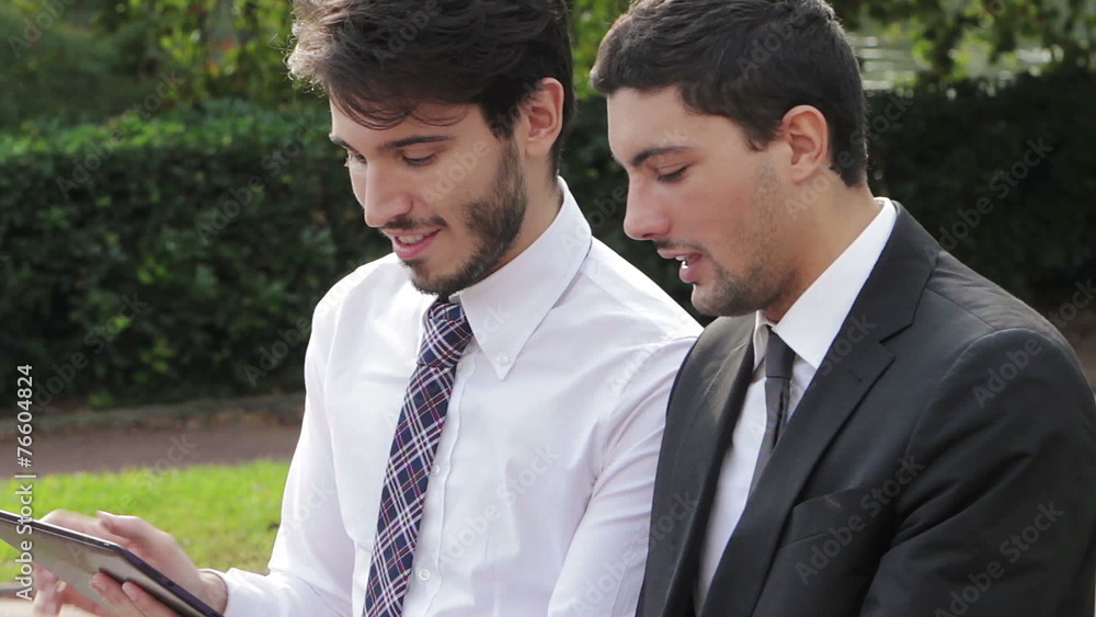 Two businessmen looking at the tablet computer on a park bench Two businessmen looking at the tablet computer on a park bench