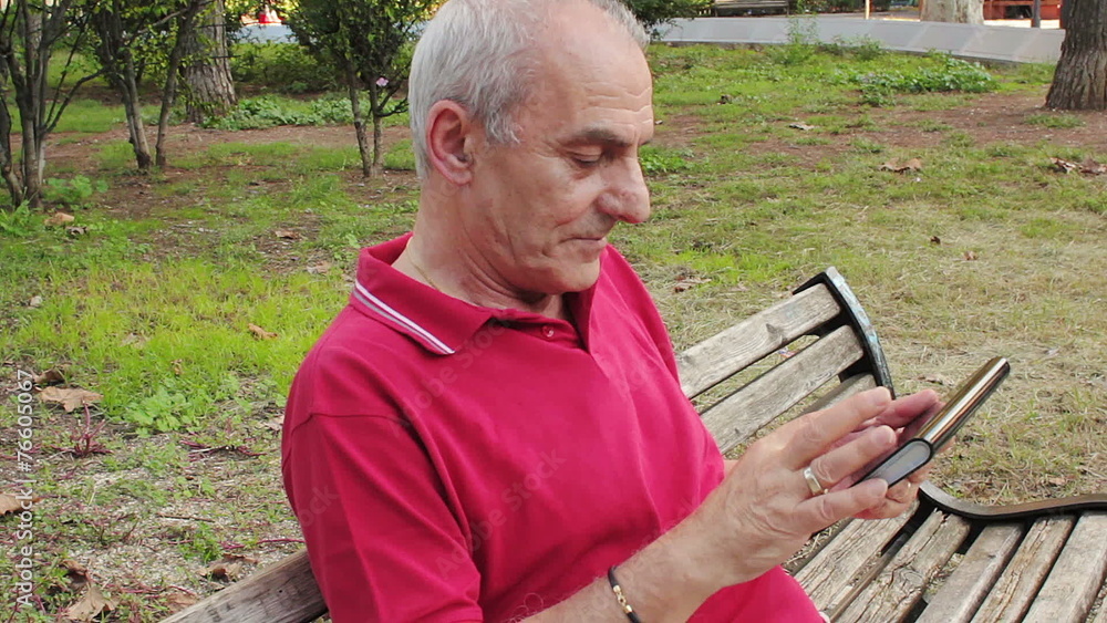 Retired senior man resting and using his tablet at table in park Retired senior man resting and using his tablet at table in park