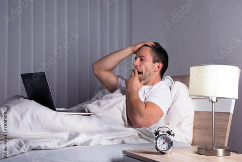 Man With Laptop On Bed Yawning