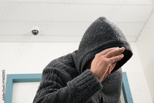 Man In Hooded Sweatshirt With Cctv Camera Behind photo